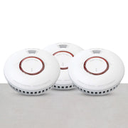 A set of three white round smoke detectors with red circles in the center, arranged on a neutral background.