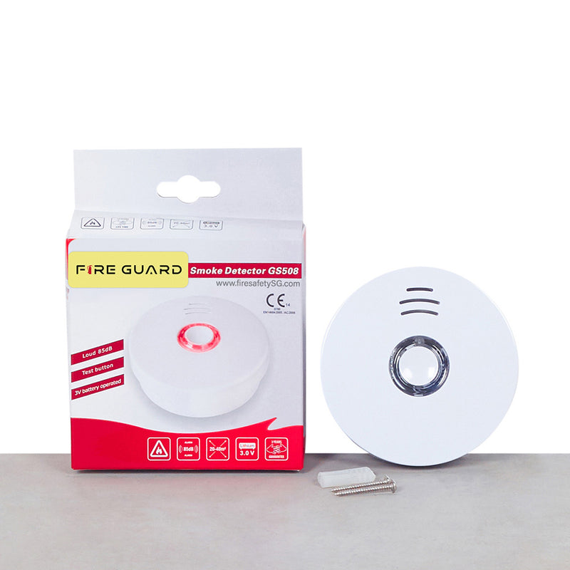 A white magnetic base with self-adhesive next to its packaging, which is labeled as 'FIRE GUARD SMOKE DETECTOR G5508'.