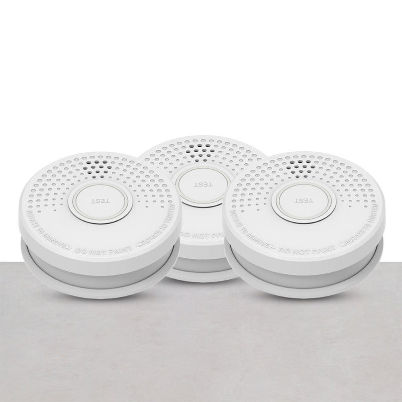 Three white smoke detectors with a circular design and a central button, placed against a grey background.