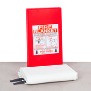 Red fire blanket in a case, with instructions label, alongside a rolled up white blanket with black stripes.